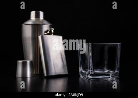 Shaker en métal, hip flask et verre de vodka. Accessoires Barman sur la table. Fond noir. Banque D'Images