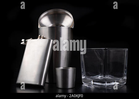 Shaker en métal, hip flask et verre de vodka. Accessoires Barman sur la table. Fond noir. Banque D'Images