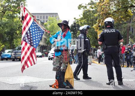 Un homme tenant un drapeau à l'envers à côté de la police à la grève du climat rassemblement à Eugene, Oregon, USA. Banque D'Images