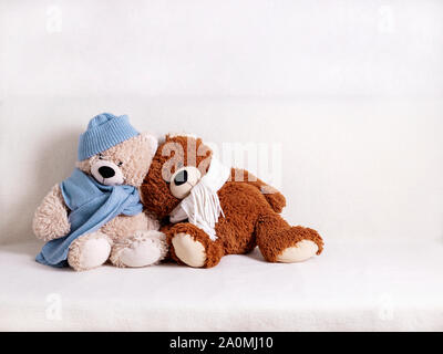 Les jouets d'ours en peluche assis sur un canapé blanc dans une écharpe en tricot blanc et bleu et un chapeau. Focus sélectif. Banque D'Images