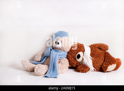 Les jouets d'ours en peluche assis sur un canapé blanc dans une écharpe en tricot blanc et bleu et un chapeau. Focus sélectif. Banque D'Images