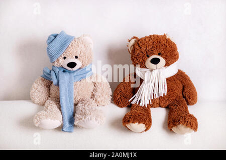 Les jouets d'ours en peluche assis sur un canapé blanc dans une écharpe en tricot blanc et bleu et un chapeau. Focus sélectif. Banque D'Images