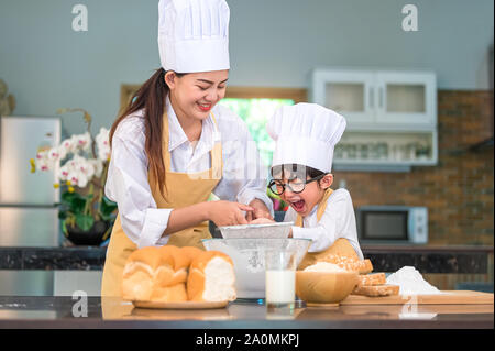 Adorable petit garçon asiatique et belle mère tamisant la farine pâte avec tamis tamis passoire dans accueil cuisine à table pour se préparer à la boulangerie et ca Banque D'Images