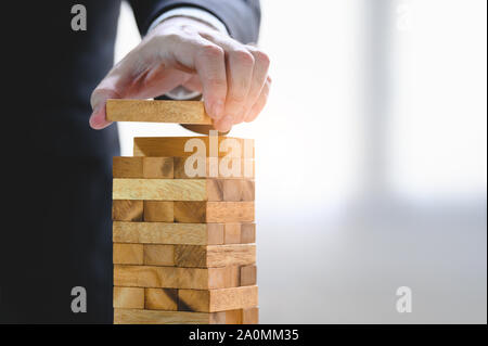 Businessman organisant la cale en bois et d'empilement de tour à la main. Organisation de l'entreprise et la croissance de l'entreprise de progrès. Succès de la stratégie et de l'argent enq Banque D'Images