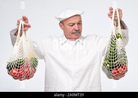 Senior hispanic cook chef holding eco blanc Ficelle en coton sacs remplis de légumes de l'épicerie et la préparation des aliments pour contrôler leur qualité Banque D'Images