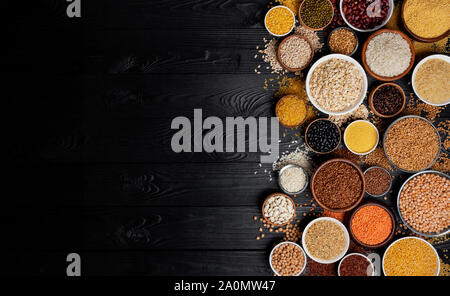 Diverses céréales, céréales, graines, gruaux, les légumineuses et les haricots dans des bols, régime riche en fibres concept, vue de dessus du porridge collection sur un parquet en bois noir backgroun Banque D'Images