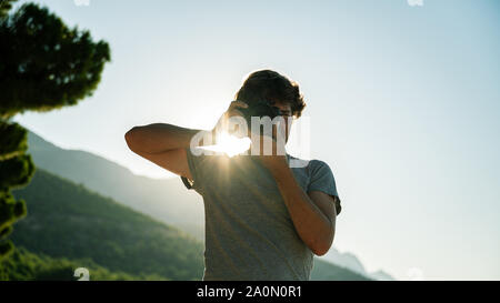 Low angle view of male photo photographe prenant directement à vous à l'extérieur avec soleil levant glowing derrière lui. Banque D'Images