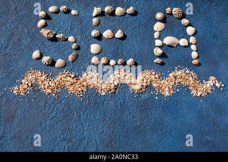 Mot mer fait de coquillages, décoratives océan vagues, du sable doré sur fond bleu top view close up, des lettres fait de coquillages, vacances d'été Banque D'Images