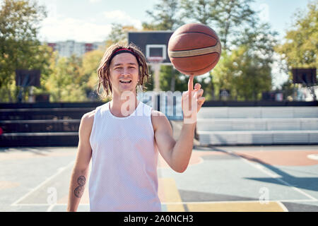 Image de l'homme sportif en T-shirt blanc avec balle dans ses mains sur jeux pour enfants en après-midi d'été Banque D'Images