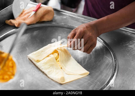 La cuisine thaï traditionnelle fried banana pancakes roti, gros plan de préparation des aliments de rue d'Asie en Thaïlande, l'homme chef de friture sur les mains des crêpes crêpière Banque D'Images