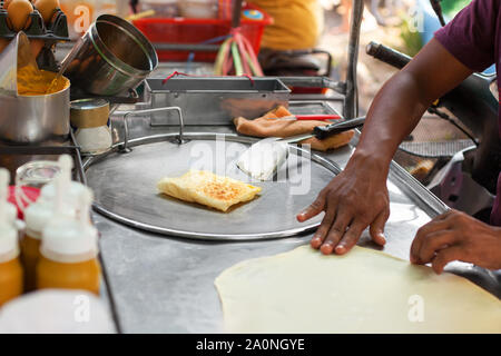 La cuisine thaï traditionnelle fried banana pancakes roti, gros plan de préparation des aliments de rue d'Asie en Thaïlande, l'homme chef de friture sur les mains des crêpes crêpière Banque D'Images