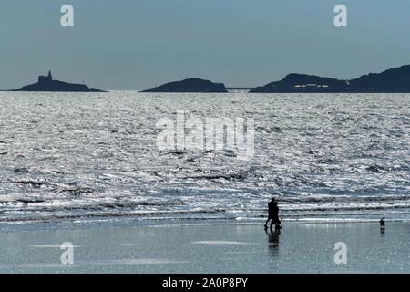 Swansea, Pays de Galles, Royaume-Uni. Samedi, 21 septembre 2019. Le soleil brille sur la mer de la Baie de Swansea, dans le sud du Pays de Galles, Royaume-Uni, comme deux personnes marcher leur chien sur le sable, sur ce qu'on croit être le dernier jour d'été au Royaume-Uni. La météo est attribuable au changement dans les prochains jours, alors que de fortes précipitations dans les prévisions pour rouler dans de l'Atlantique et de mettre un terme à l'été indien au cours de la semaine dernière. Crédit photo : Robert Melen/Alamy Live News. Banque D'Images