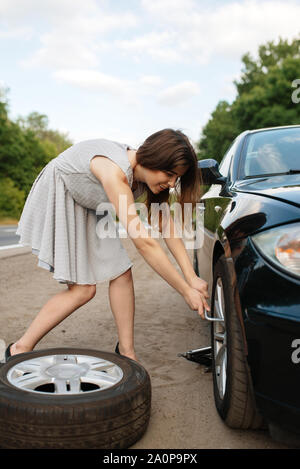 Panne de voiture, la jeune femme met le pneu de rechange Banque D'Images