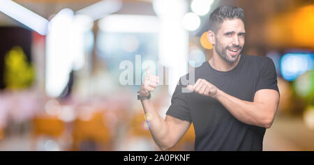 Jeune homme séduisant sur fond isolé en pointant sur l'arrière derrière avec la main et Thumbs up, souriant confiant Banque D'Images