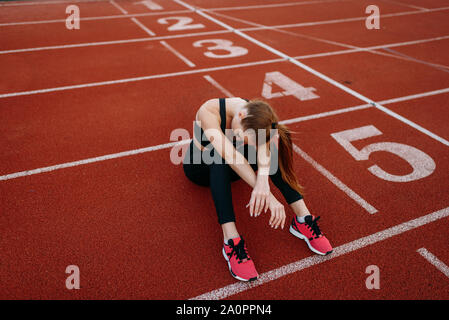 Fatigué female jogger assis sur le sol, le stade Banque D'Images