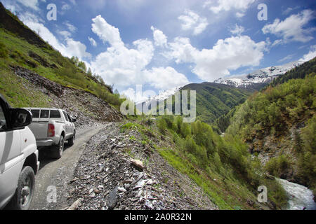 Deux voitures sur une route serpentine dans les montagnes, des pics de montagne dans la neige et l'arrière-plan de Green Hills Banque D'Images