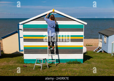 Éoliennes offshore avec une femme peinture sa cabane de plage au premier plan, près de Hastings sur la côte du Kent à la fin de l'été Banque D'Images