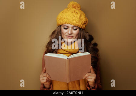 Happy young woman in yellow beret et écharpe reading book contre fond beige. Banque D'Images