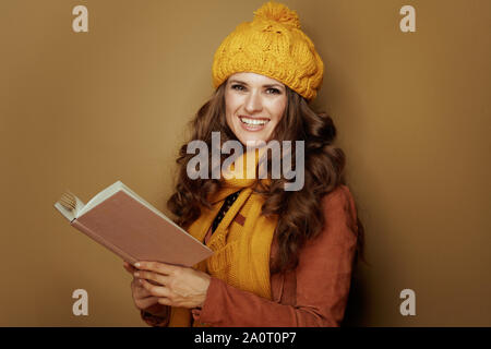 Femme élégante heureux en béret et écharpe jaune livre lecture isolé sur fond de bronze. Banque D'Images