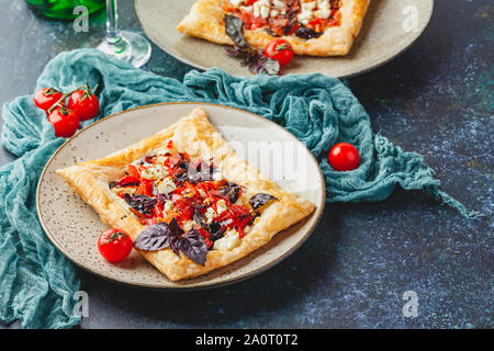 Tartelettes de pâte feuilletée avec tomates, poivrons doux, salami, fromage feta et basilic pourpre. Banque D'Images