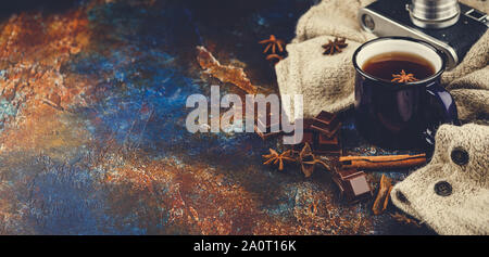 Émaillé bleu tasse de thé, des bâtons de cannelle, d'anis étoile, morceaux de chocolat noir, pull en laine chaude et rétro caméra sur un fond sombre. L'espace pour tex Banque D'Images