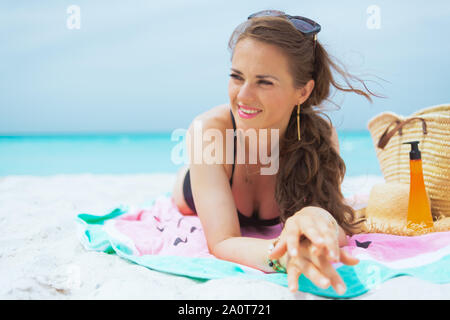 Heureux âge moyen élégant femme aux longs cheveux bouclés dans un élégant maillot noir sur une plage de sable blanc de soleil. Banque D'Images