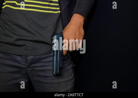 Asian man détient une arme à feu. Fusil à la main isolé sur fond noir. Banque D'Images