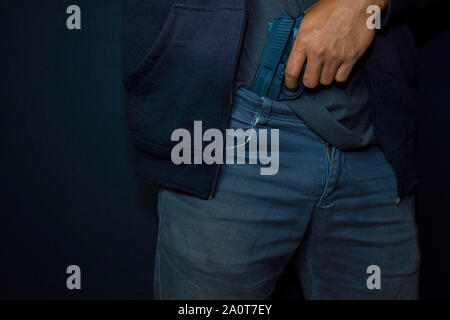 Asian man détient une arme à feu. Pistolet dans son pantalon isolé sur fond noir. Banque D'Images