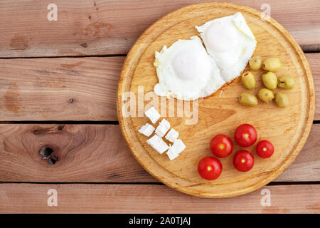 Des œufs au plat, œufs brouillés, fromage, olives et tomates sur plateau en bois sur fond de bois. Le turc, le petit-déjeuner méditerranéen Banque D'Images