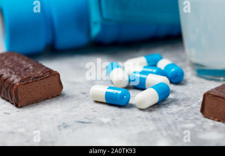 Bar à haute teneur en protéines, BCAA (acides aminés) Verre, Creatine Capsules haltère et bleu en arrière-plan. Nutrition sportive. Arrière-plan de pierre. Close up. Banque D'Images