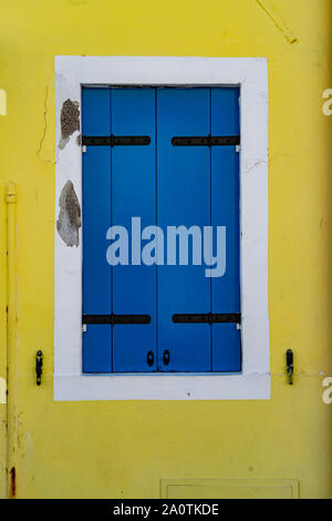 Obturateur bleu sur un mur jaune. Maisons colorées sur l'île de Burano, Italie Banque D'Images