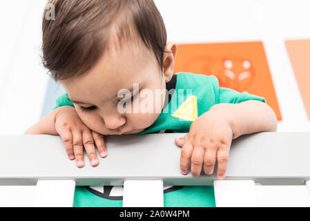 Bébé debout et se tenant à la rambarde du lit. Portant un t-shirt vert mignon dans une pépinière moderne et minimaliste lumineux chambre à coucher. Banque D'Images