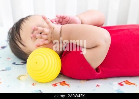 Bébé jouant avec des balles en caoutchouc jouets dans le lit dans une salle lumineuse. Enfant portant une robe rouge, portant sur la feuille de huche de dinosaure ludique. Banque D'Images