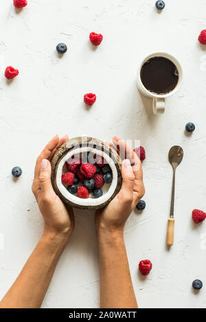 Mise à plat de la nourriture. Les baies fraîches et de noix de coco, tasse de café, les mains Banque D'Images