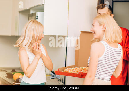 Pizza delivery man a commander une pizza pour les clients à la maison. Deux jeunes femmes blonde joyeuse satisfait de la livraison rapide de pizzas, ils ont le sourire et laug Banque D'Images