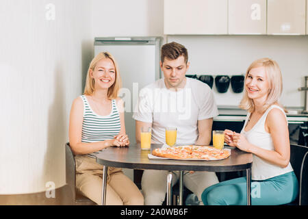 L'amitié, les gens et la société food concept. Trois étudiants heureux caucasienne eating pizza dans la cuisine.Ils ont de la partie à la maison, riant et s'amusant, le dr Banque D'Images