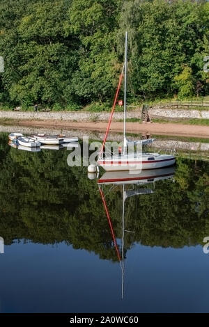 Un seul bateau à voile sur un lac avec des reflets dans l'eau. La location et avec trois petites barques amarrées aussi derrière Banque D'Images