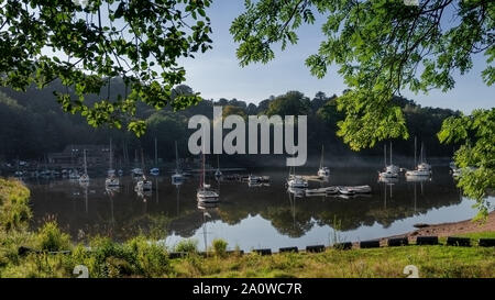 Un paysage de Rudyard Lake dans le Staffordshire. La scène est prise avec le cadrage d'arbres avec des bateaux amarrés réflexions jusqu'à la surface de l'eau Banque D'Images