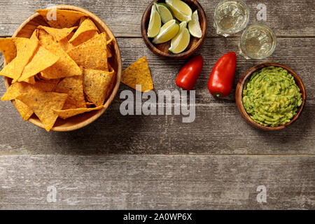 Vue de dessus de nachos servis avec du guacamole, des poivrons, des limes et de la Tequila sur table en bois patiné Banque D'Images