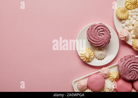 Vue de dessus de rose, blanc et jaune de meringues, macarons et des guimauves sur fond rose Banque D'Images