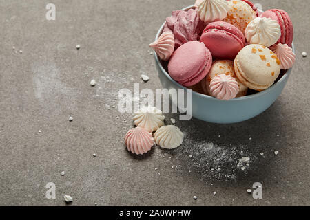 Français délicieux macarons et meringues dans bol bleu et brisé des morceaux de sucre sur fond gris Banque D'Images