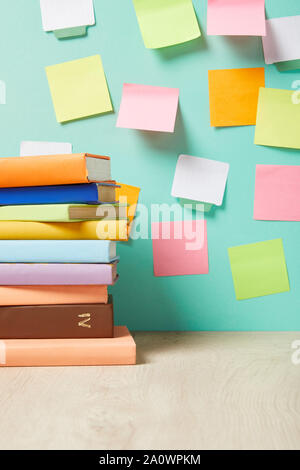 Pile de livres sur la table près de post-it multicolores sur mur turquoise Banque D'Images