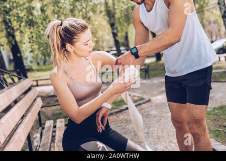 Dans l'homme sportswear le bandage coude blessé de la sportive jeunes assis sur un banc dans le parc Banque D'Images