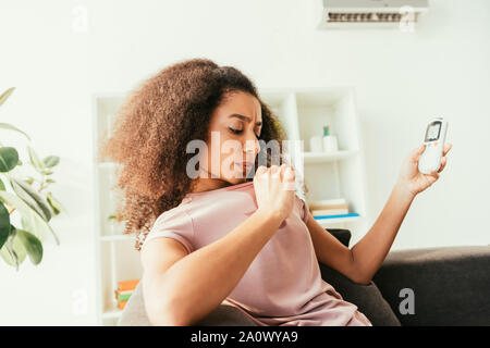 Young african american woman holding shirt transpirant à télécommande de climatiseur Banque D'Images