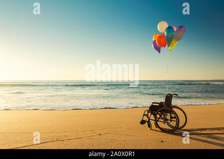 Wellchair sur une plage avec des ballons de couleur Banque D'Images