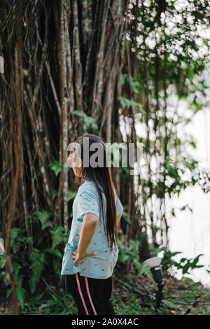 Peu cute child girl Standing alone avec près de Banyan Tree Banque D'Images