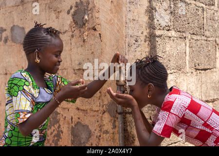 Deux filles heureusement le partage de l'eau de robinet à Bamako, Mali Banque D'Images