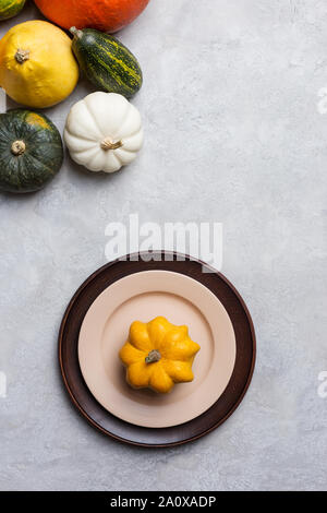 Assiettes vides avec citrouille jaune sur elle, la décoration des citrouilles en gauche de l'image. La récolte et l'ensemble de tables de grâces sur fond de béton gris. Haut Banque D'Images