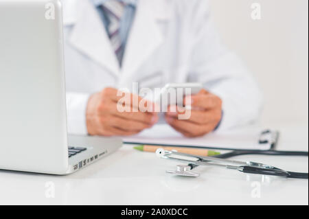 Médecin à son bureau à l'hôpital travailler close-up using laptop holding smartphone Banque D'Images