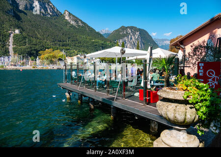 Les gens de manger au restaurant sur la plate-forme au-dessus du lac, le lac de Garde, Riva del Garda, Trentin, Haut Adige, Italie du Nord Banque D'Images